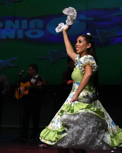 Bailarina de Kahuira con vestido floreado y pañuelo en alto sobre el escenario en Islas Canarias