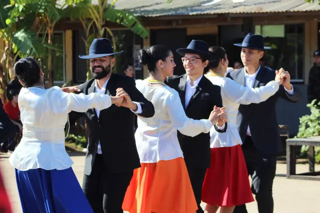 Parejas de Kahuira con vestido blanco y traje de huaso negro bailando al aire libre
